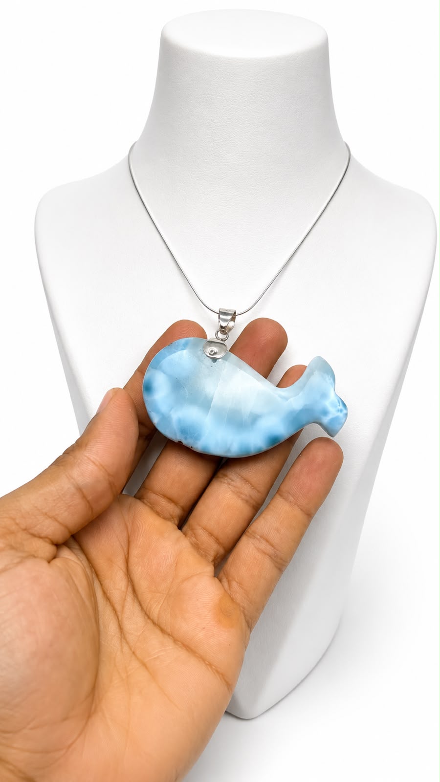 A light blue and white marbled whale-shaped pendant necklace held in a hand in front of a white mannequin bust.
