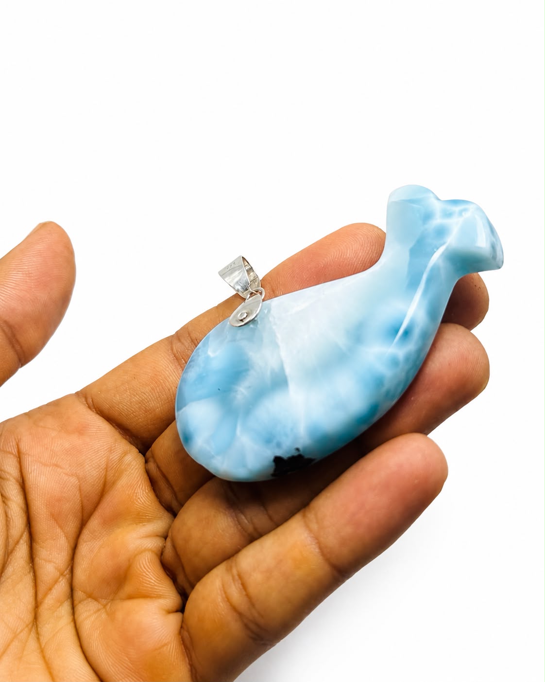 A light blue  larimar and white marbled whale-shaped pendant with a silver bail, held in a person's hand against a plain white background.