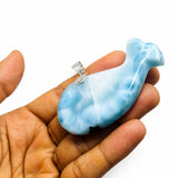 A light blue  larimar and white marbled whale-shaped pendant with a silver bail, held in a person's hand against a plain white background.