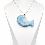 A silver necklace with a light blue and white marbled whale-shaped pendant, displayed on a white mannequin bust against a white background.
