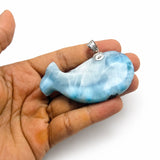 A hand holding a small blue and white marbled whale-shaped pendant with a silver bail, shown against a plain white background.