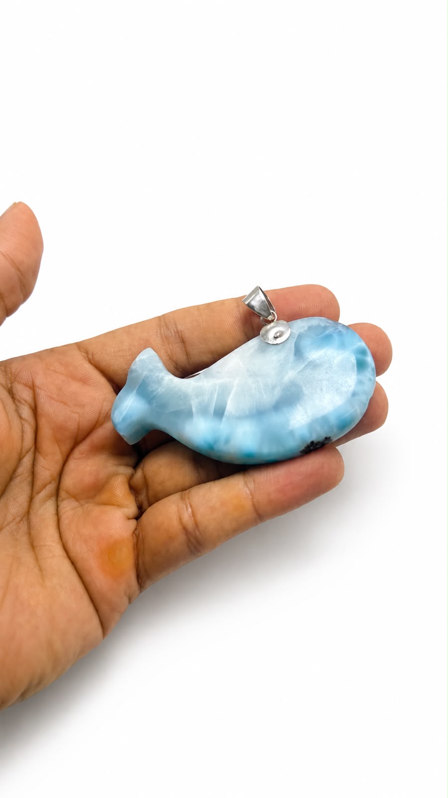 A hand holding a small blue and white marbled whale-shaped pendant with a silver bail, shown against a plain white background.