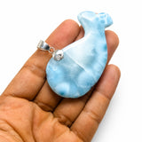 A light blue and white marbled pendant shaped like a stylized bird, held in the palm of a hand against a plain white background.