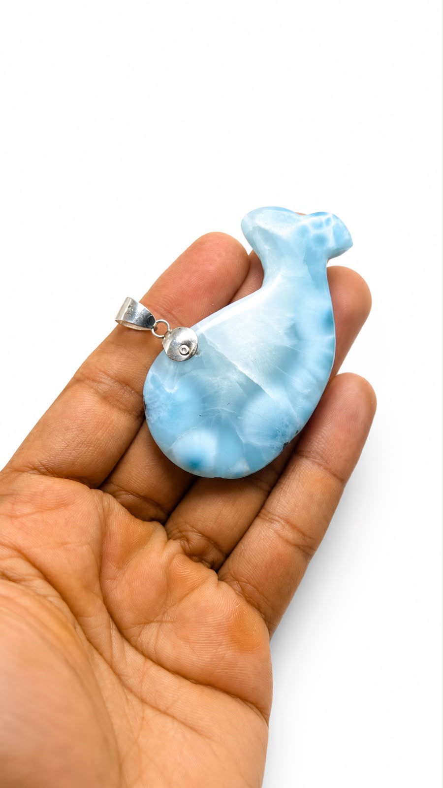 A light blue and white marbled pendant shaped like a stylized bird, held in the palm of a hand against a plain white background.