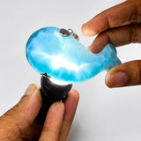 A person's hands holding a small, whale-shaped light that glows with a bright blue and white internal light, set against a plain light gray background.