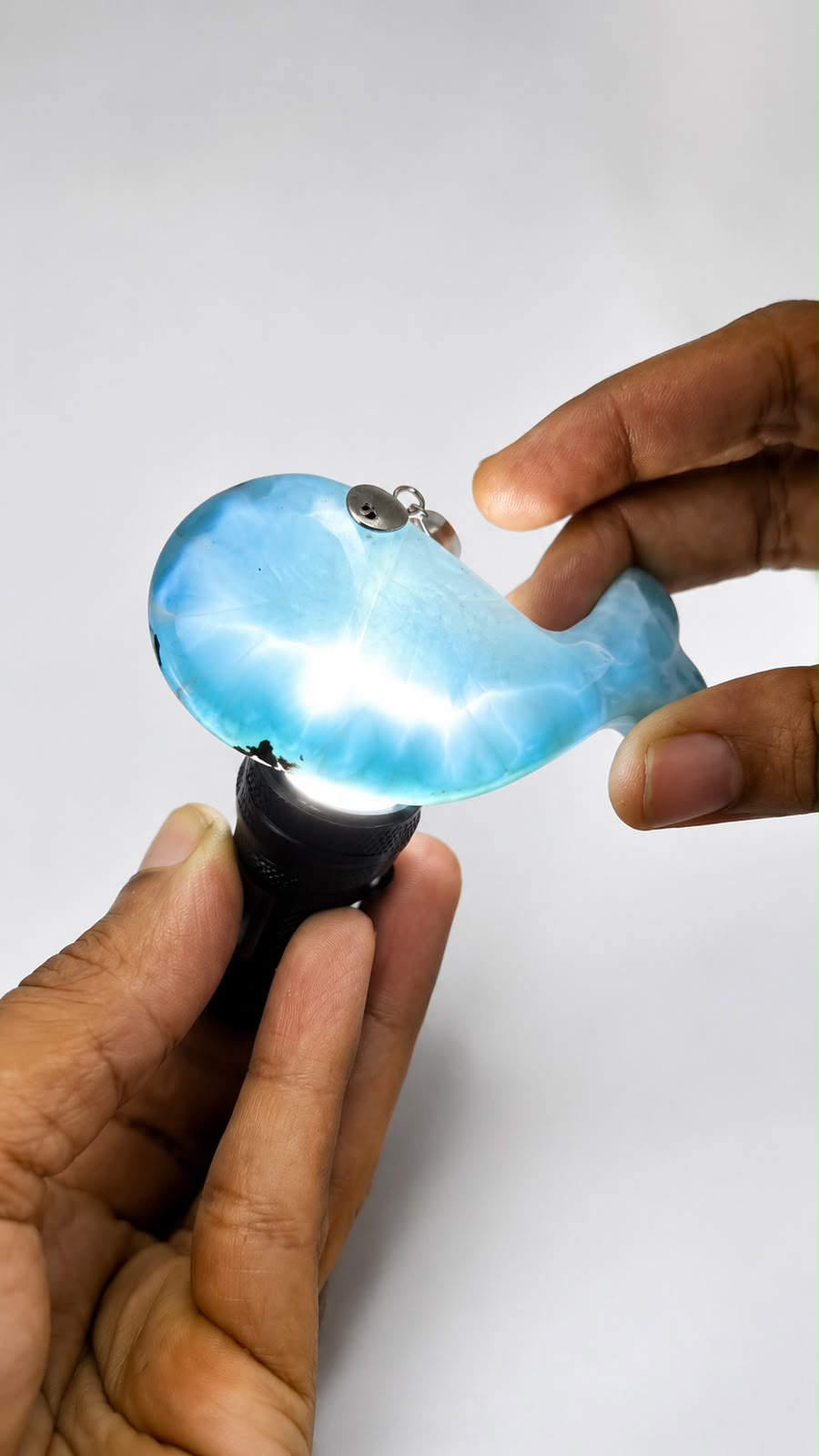 A person's hands holding a small, whale-shaped light that glows with a bright blue and white internal light, set against a plain light gray background.