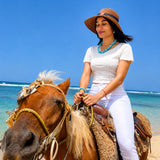 Woman riding a horse on a beach with clear blue sky and ocean with Larimar Necklace and Bracelet