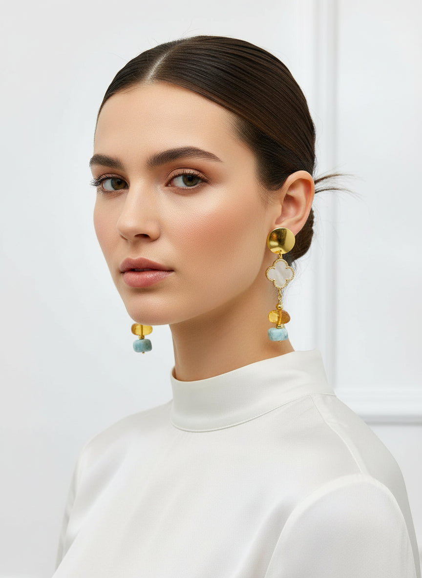 Gold earrings with turquoise and amber beads held in a hand against a rock background