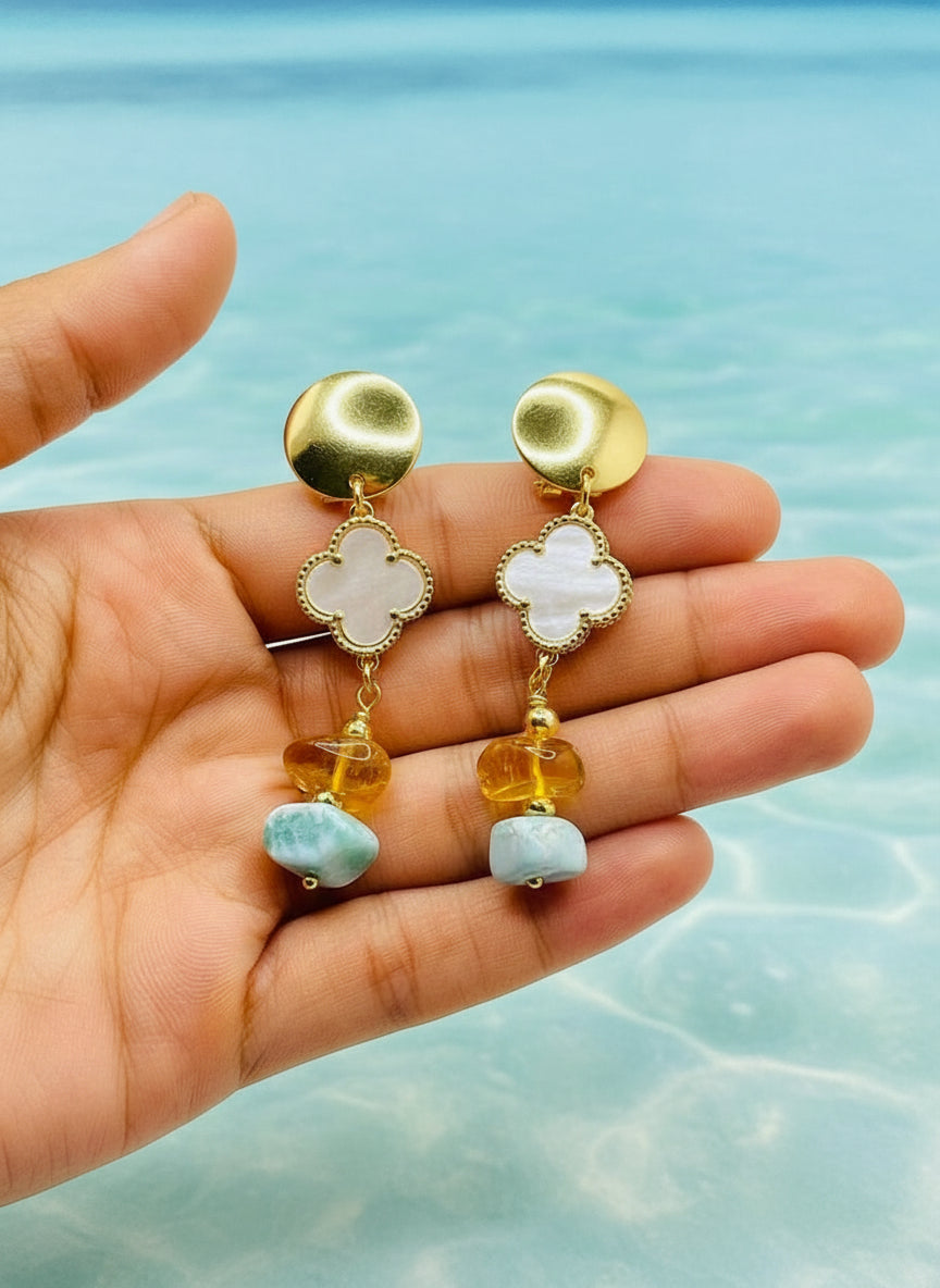 Gold earrings with gemstones held in a hand against a water background