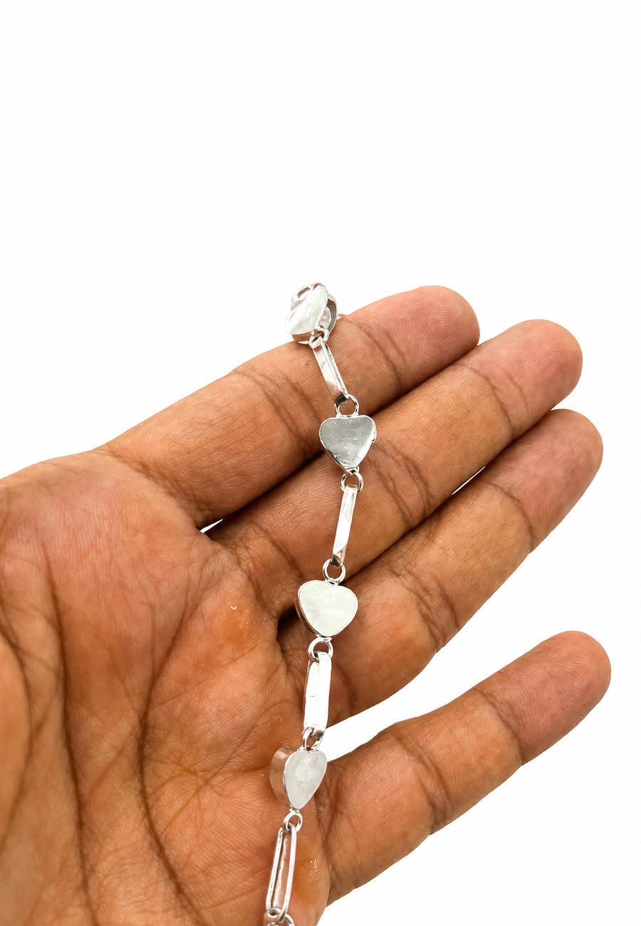A silver-toned chain bracelet with small heart-shaped links, held in a person's hand against a plain white background.