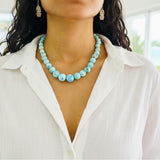 Person wearing a larimar beaded necklace with a blurred outdoor background