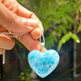 Hand holding a blue heart-shaped pendant with a blurred green background