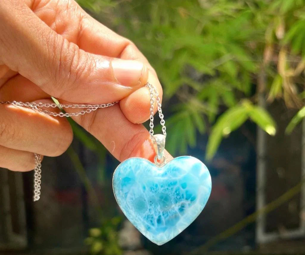 Hand holding a blue heart-shaped pendant with a blurred green background