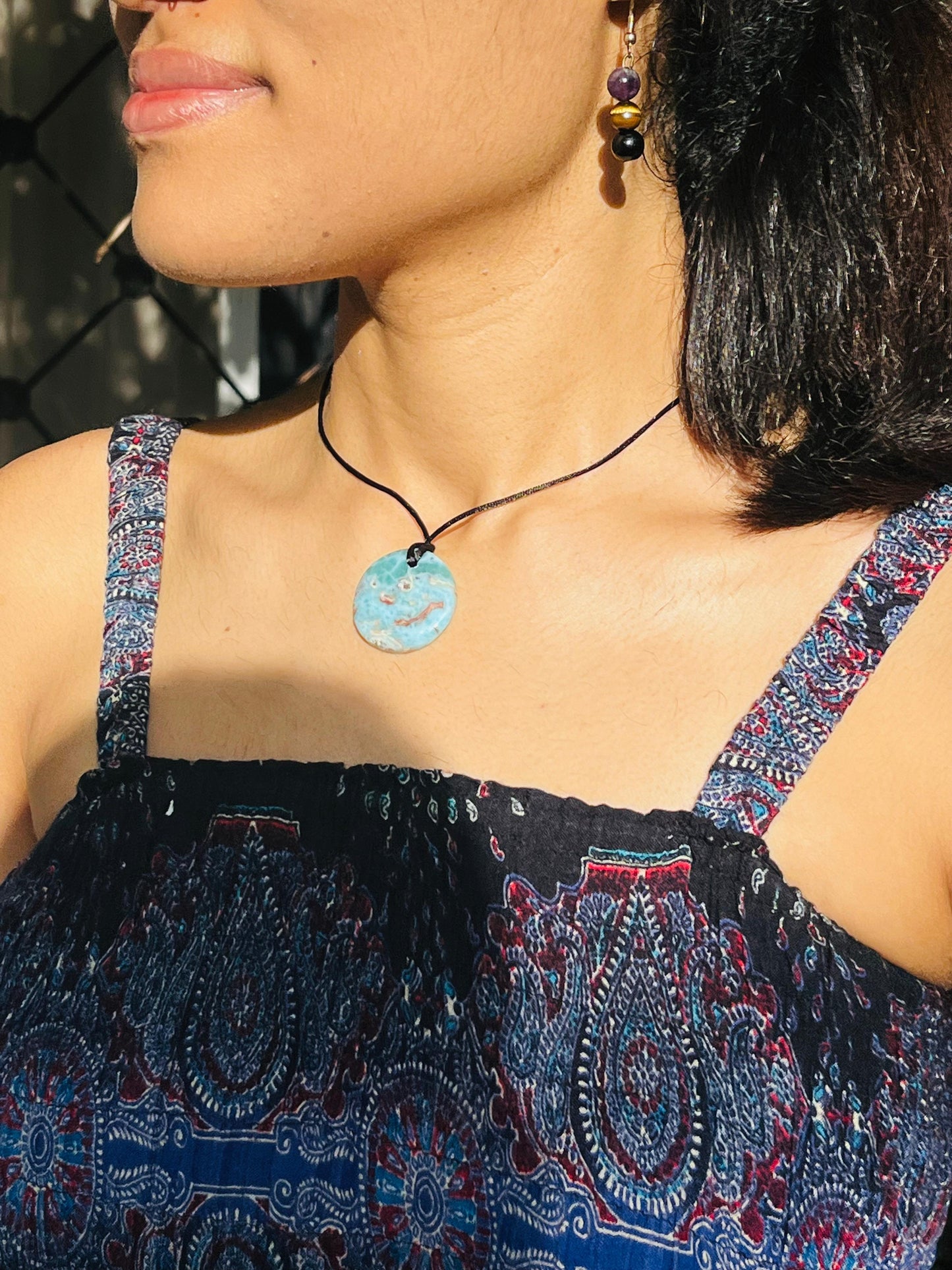 Close-up of a person wearing a blue pendant necklace with a patterned top.