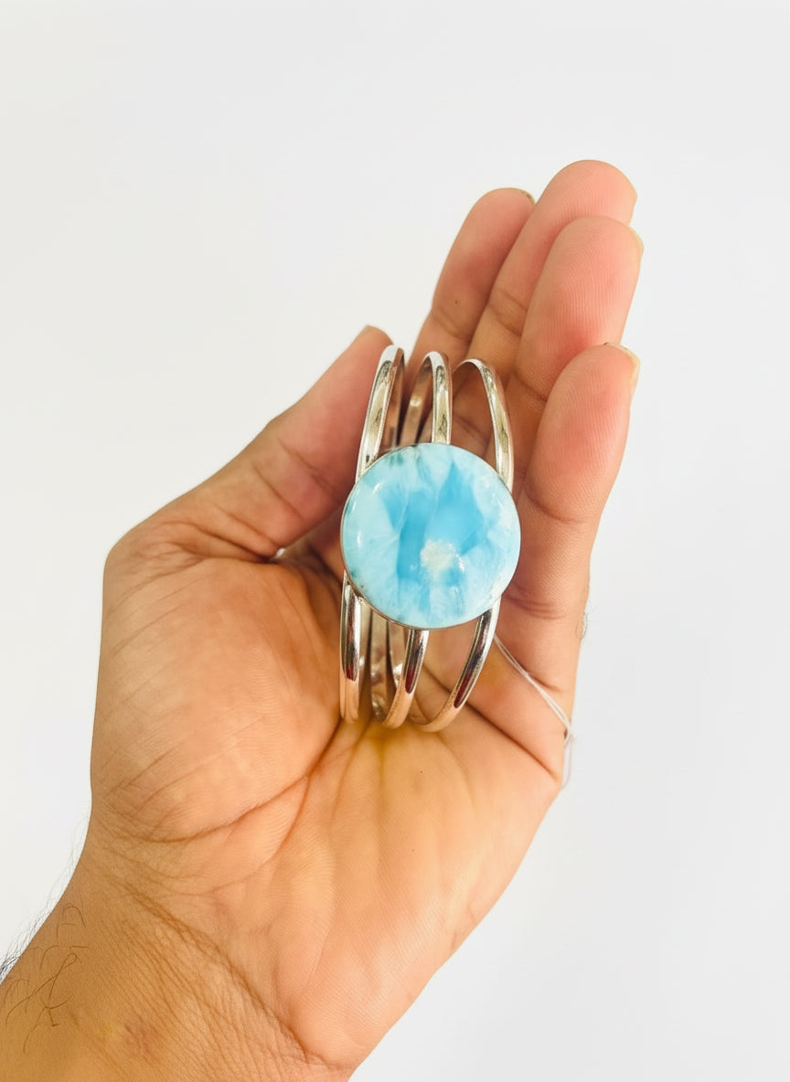 Hand holding a silver ring with a blue stone against a blurred background