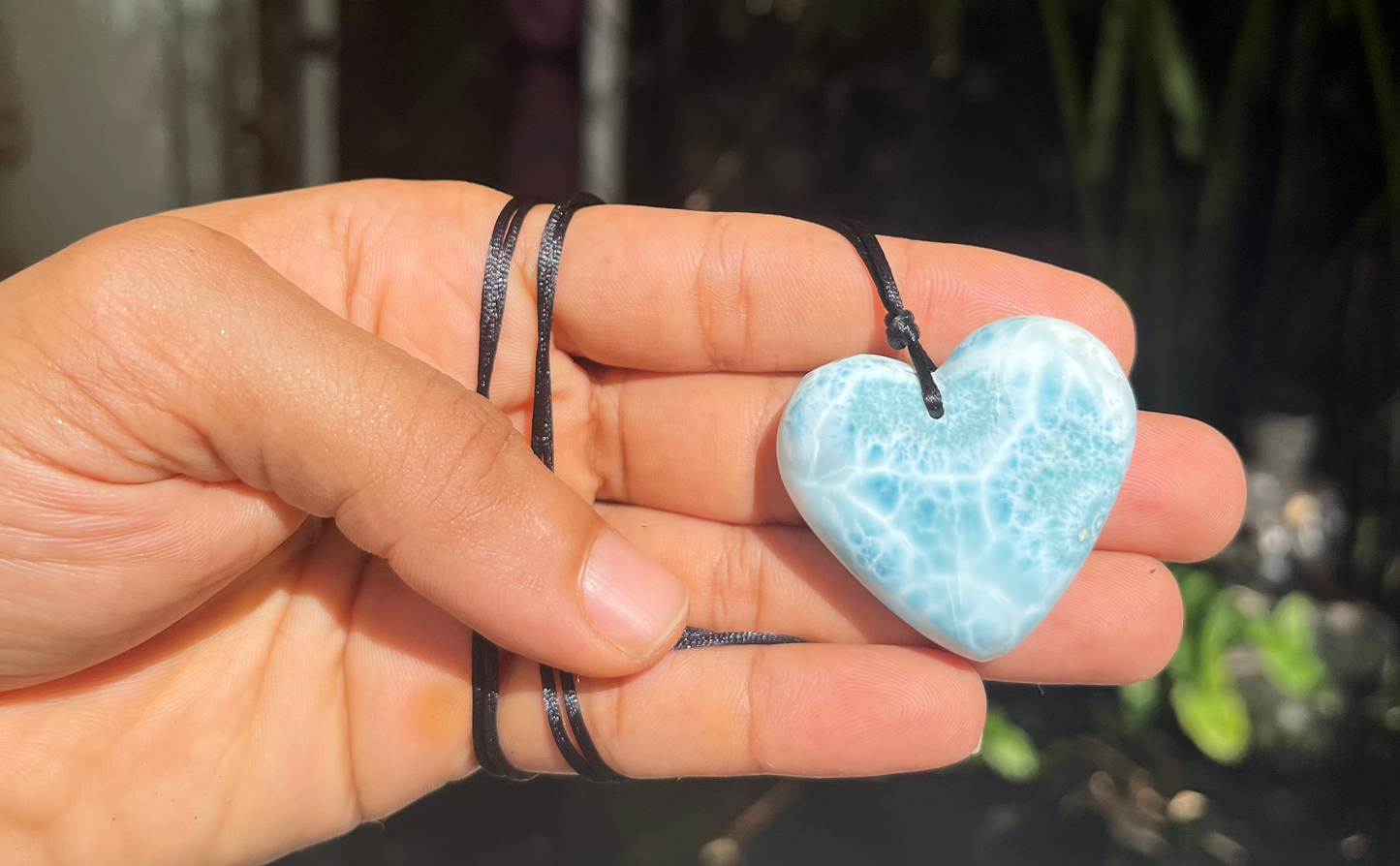 Hand holding a blue  Larimar heart-shaped pendant with a blurred background
