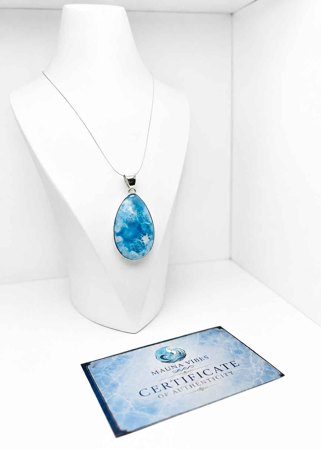A teardrop-shaped blue marbled pendant necklace displayed on a white mannequin bust, with a Certificate of Authenticity card from Mauna Voes beneath it.