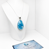 A teardrop-shaped blue marbled pendant necklace displayed on a white mannequin bust, with a Certificate of Authenticity card from Mauna Voes beneath it.