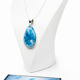 A teardrop-shaped blue and white marbled pendant necklace displayed on a white mannequin bust, with a Certificate of Authenticity card from Mauna Vibes placed in front on a white background.