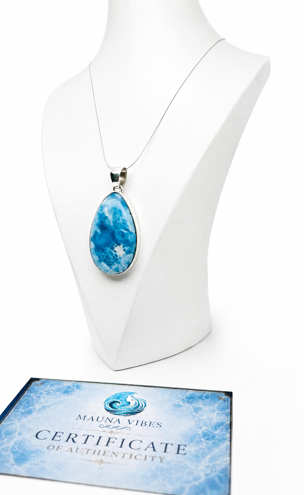 A teardrop-shaped blue and white marbled pendant necklace displayed on a white mannequin bust, with a Certificate of Authenticity card from Mauna Vibes placed in front on a white background.