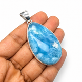 A silver oval pendant with a marbled blue and white stone, held in a person's hand against a plain white background.