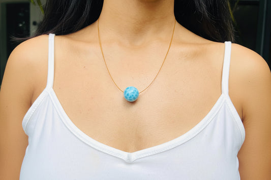 Person wearing a necklace with a blue pendant, blurred background