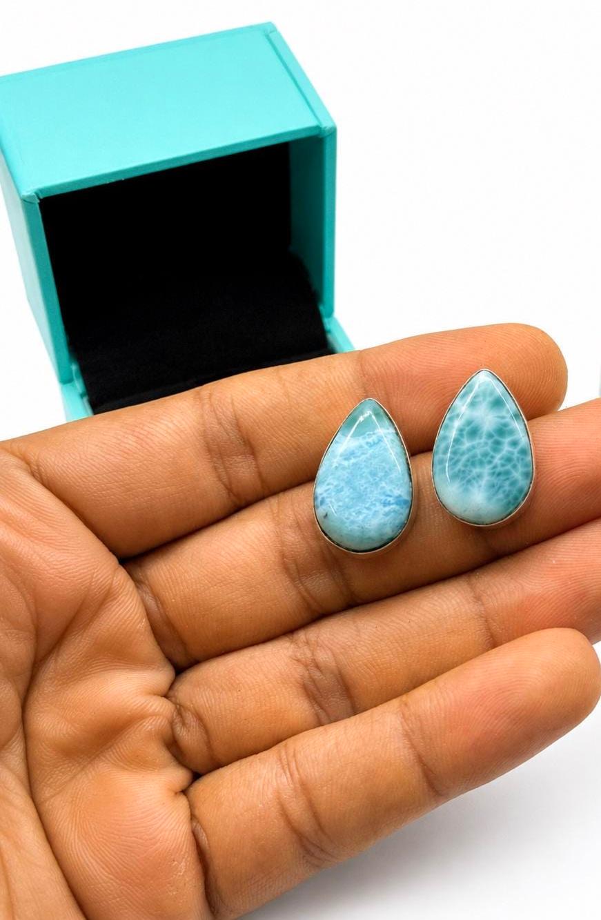 Hand holding Natural Larimar teardrop stud earrings handcrafted in solid 925 sterling silver with genuine Dominican Larimar gemstones displayed in a luxury jewelry gift box.