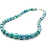 A beaded larimar necklace made of round turquoise-blue and green marbled beads with a small gold clasp, displayed on a clean white background.