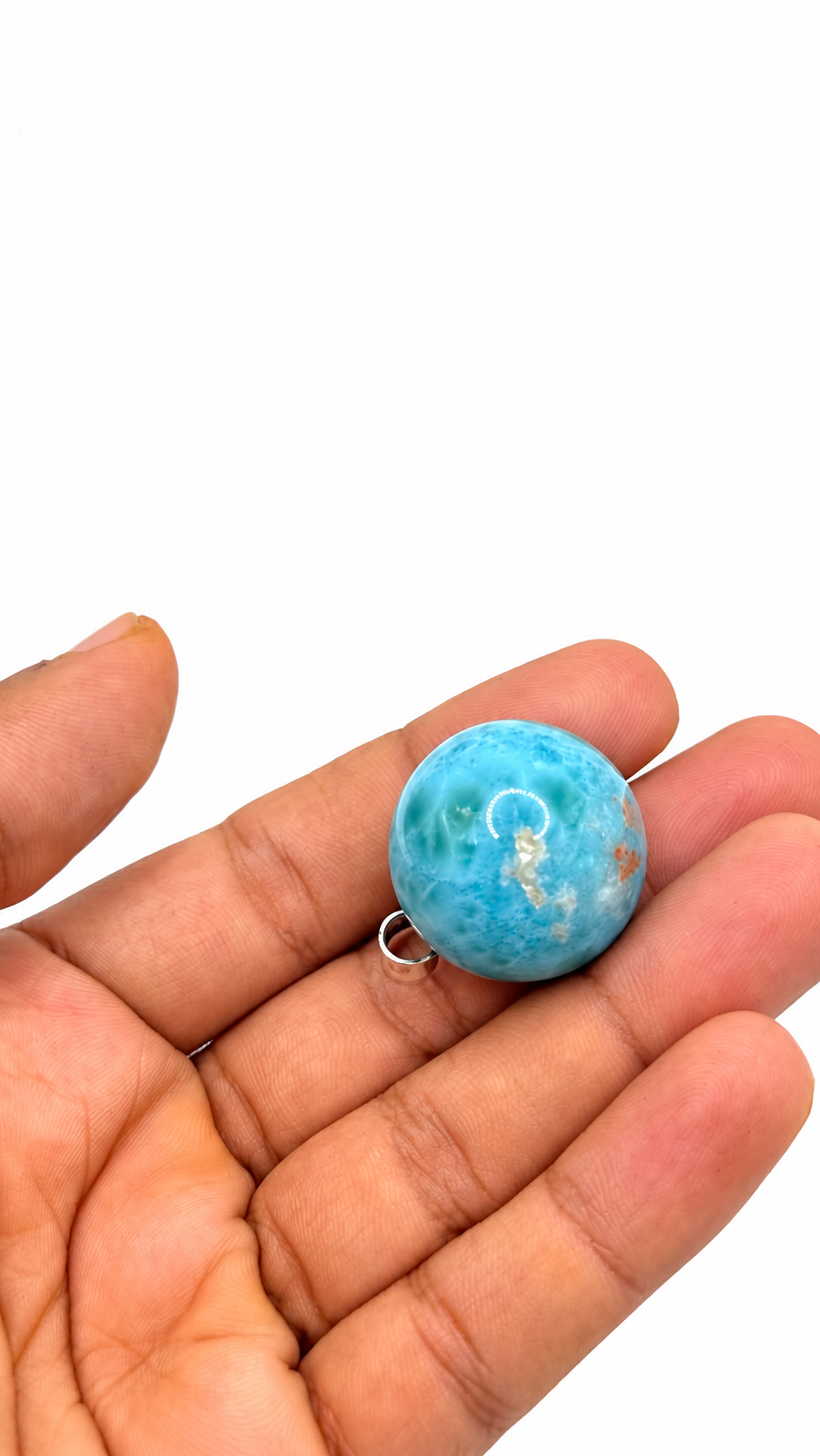 A round turquoise-blue stone bead with a small silver jump ring, held in the palm of a hand against a plain white background.