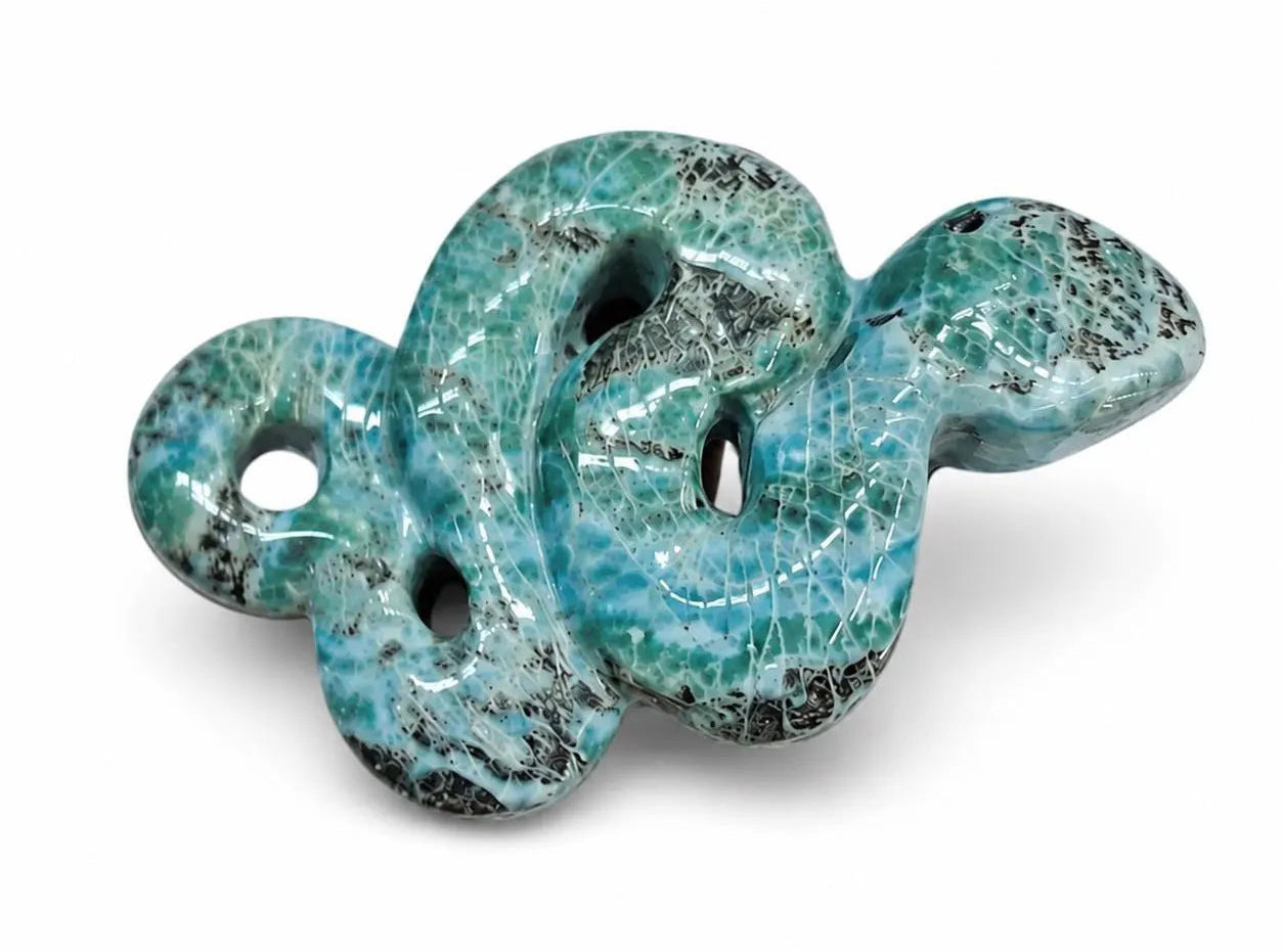 A carved  Larimar stone shaped like a coiled snake, featuring a glossy turquoise and teal body with prominent black and dark gray veining, set against a plain white background.