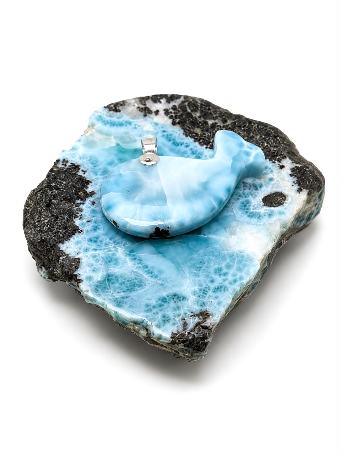 A whale-shaped pendant in light blue and white marbled resin, displayed on a decorative black and white marbled stone base against a white background.
