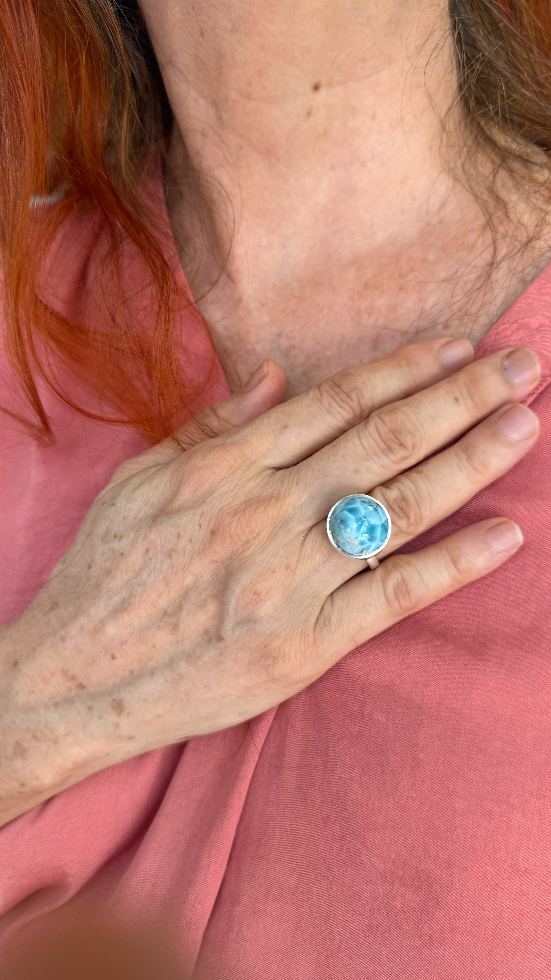 A close-up of a person wearing a silver ring with a round larimar ring