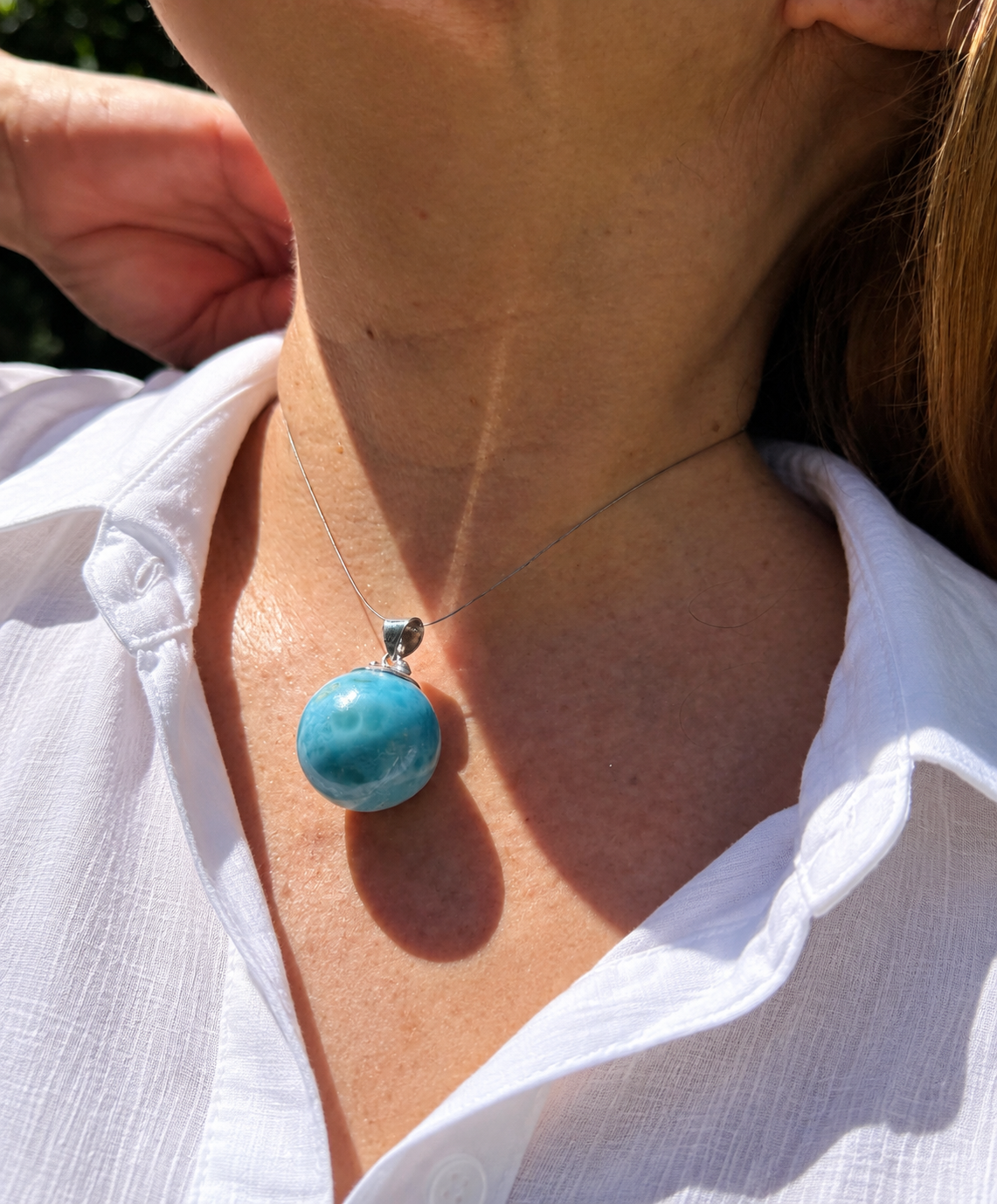 A close-up of a person wearing a silver larimar necklace