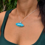 A close-up lifestyle shot of a woman wearing a silver necklace with a vibrant blue marbled labradorite pendant, paired with a dark green ribbed tank top.