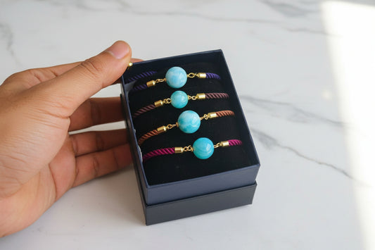 Hand holding a small box with blue beads and red strings against a blurred background