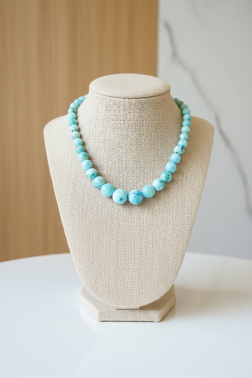 Person wearing a blue beaded necklace and a checkered top.
