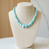 Person wearing a blue beaded necklace and a checkered top.