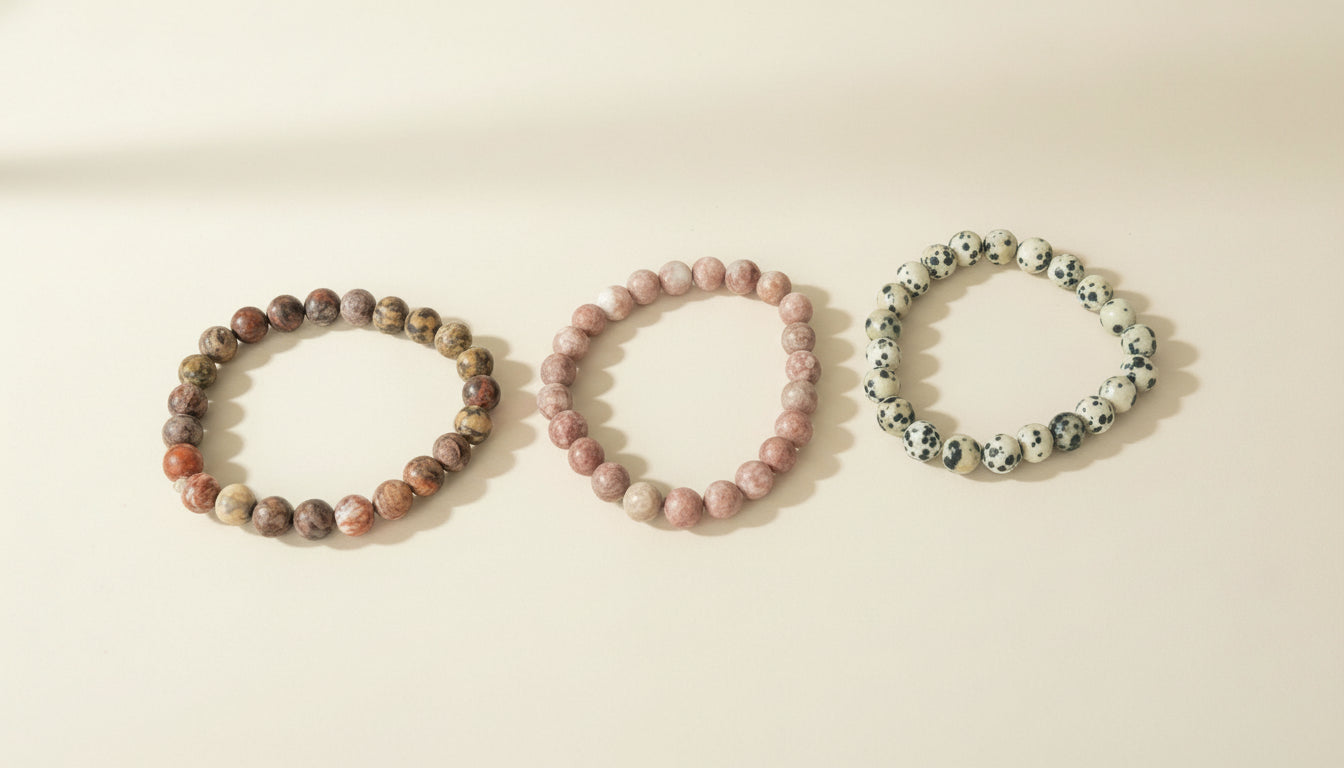 Three beaded bracelets labeled 'Leopard Jasper', 'Rhodonite', and 'Dalmatian Jasper' on a beige background.