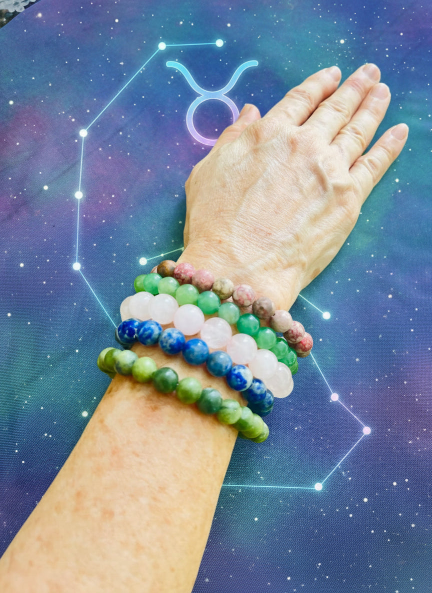 Hand wearing multiple beaded bracelets on a green fabric background