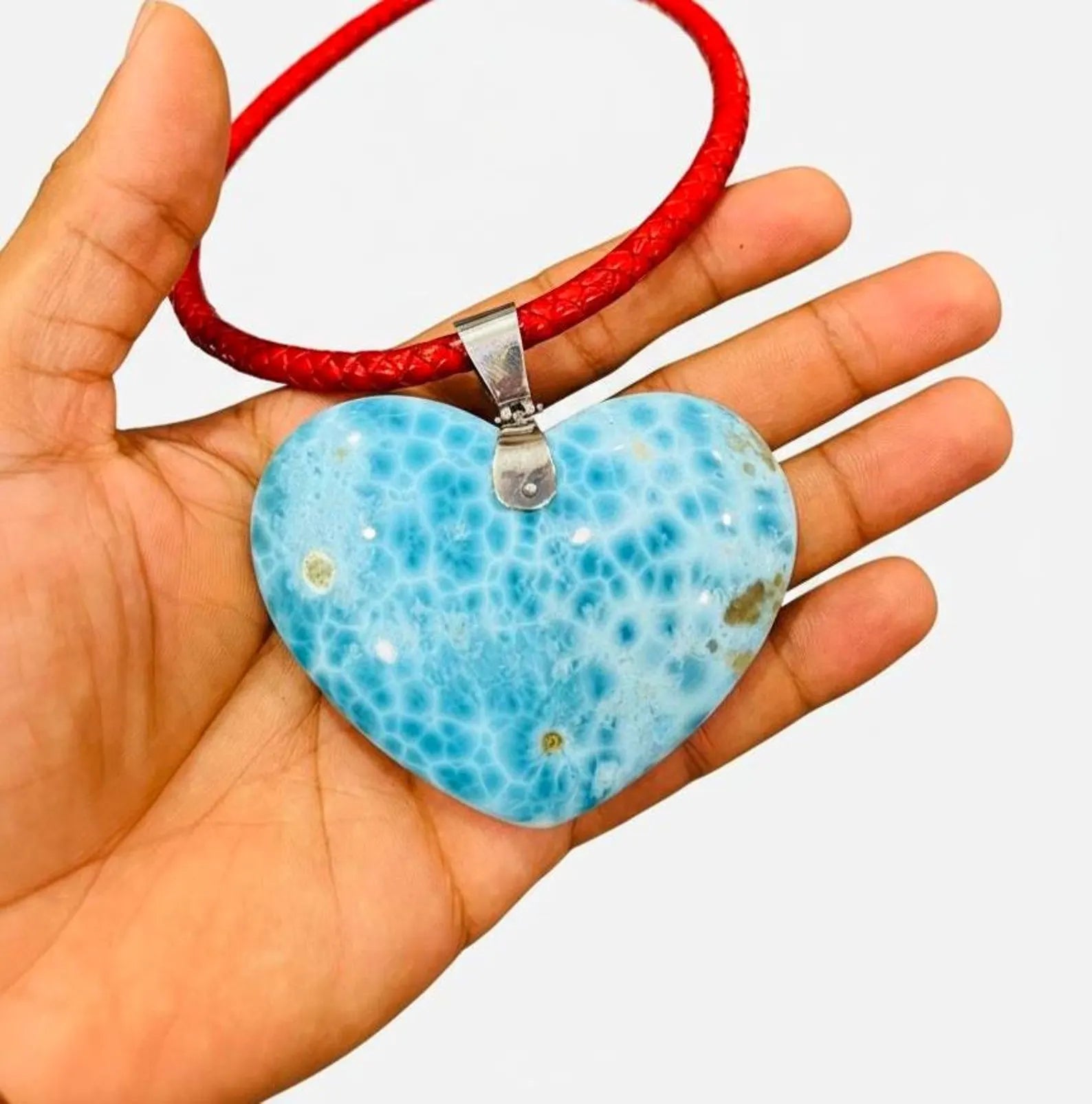 Hand holding a Larimar  heart-shaped Necklace pendant on a red cord against a white background