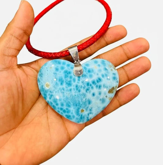 Hand holding a Larimar  heart-shaped Necklace pendant on a red cord against a white background