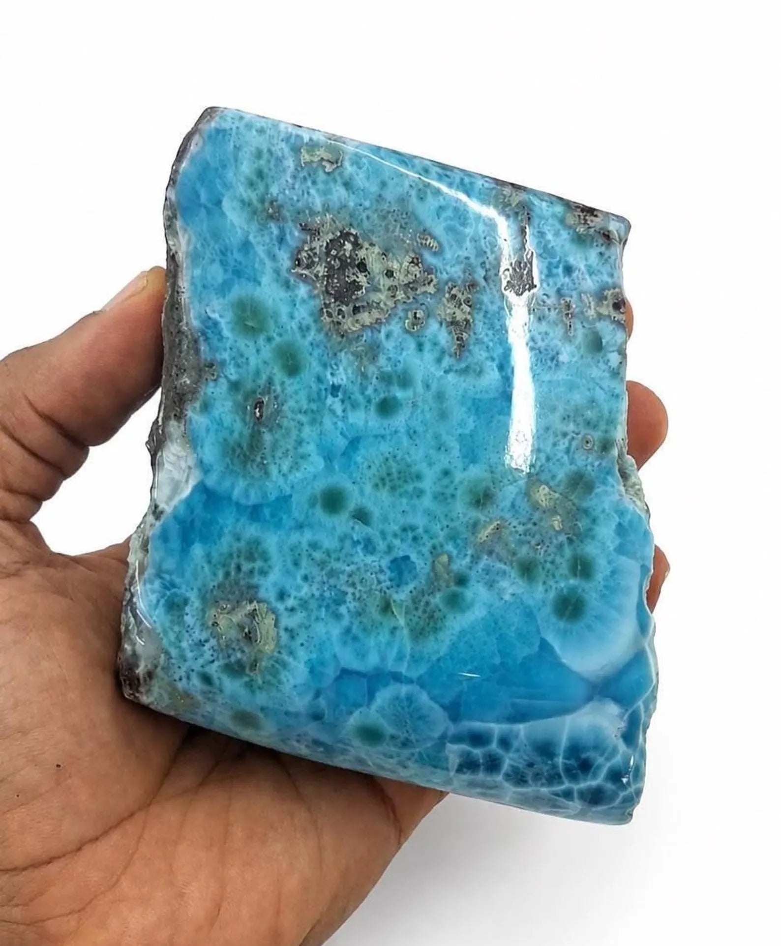 A hand holding a polished blue Larimar stone slab with natural mottled patterns and rough edges against a plain white background.