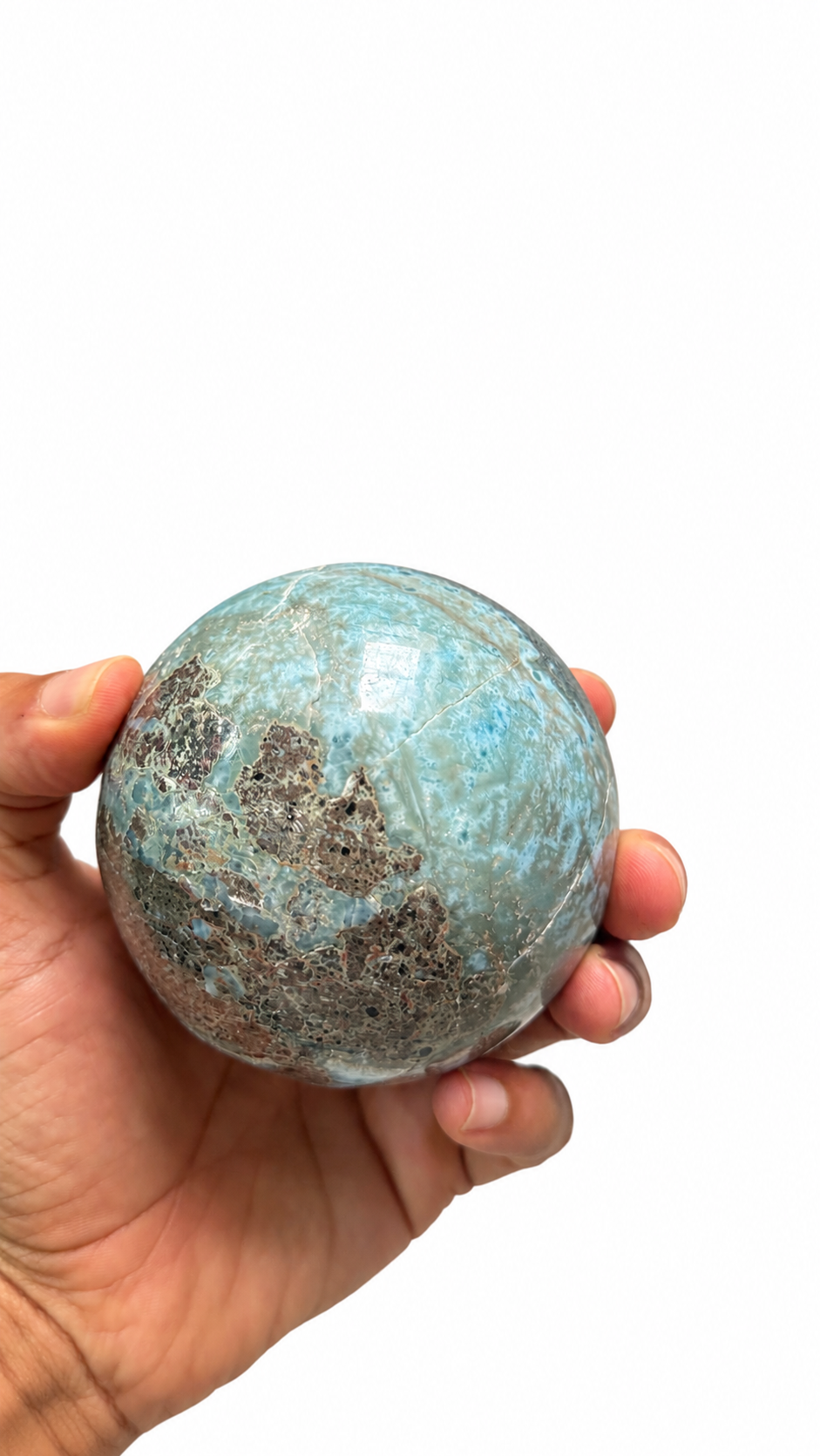 A hand holding a polished turquoise-blue and brown stone sphere against a plain white background.