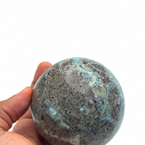 A hand holding a polished round larimar stone sphere 
