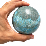 A hand holding a polished larimar sphere 