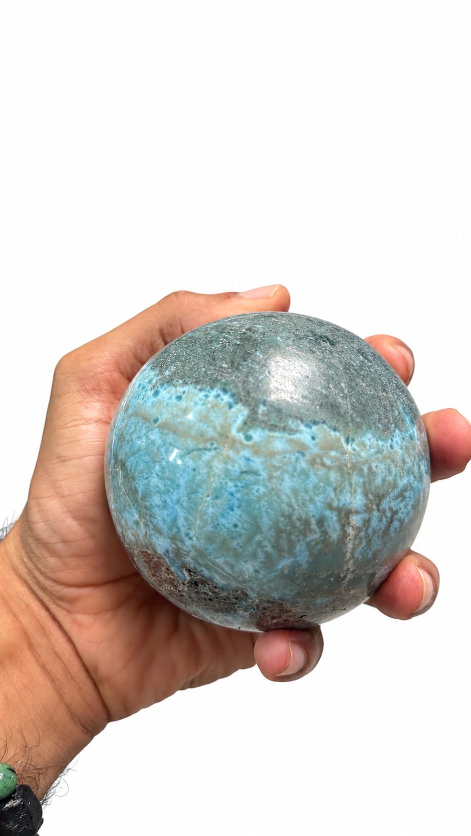 A hand holding a polished blue-green stone sphere against a plain white background.