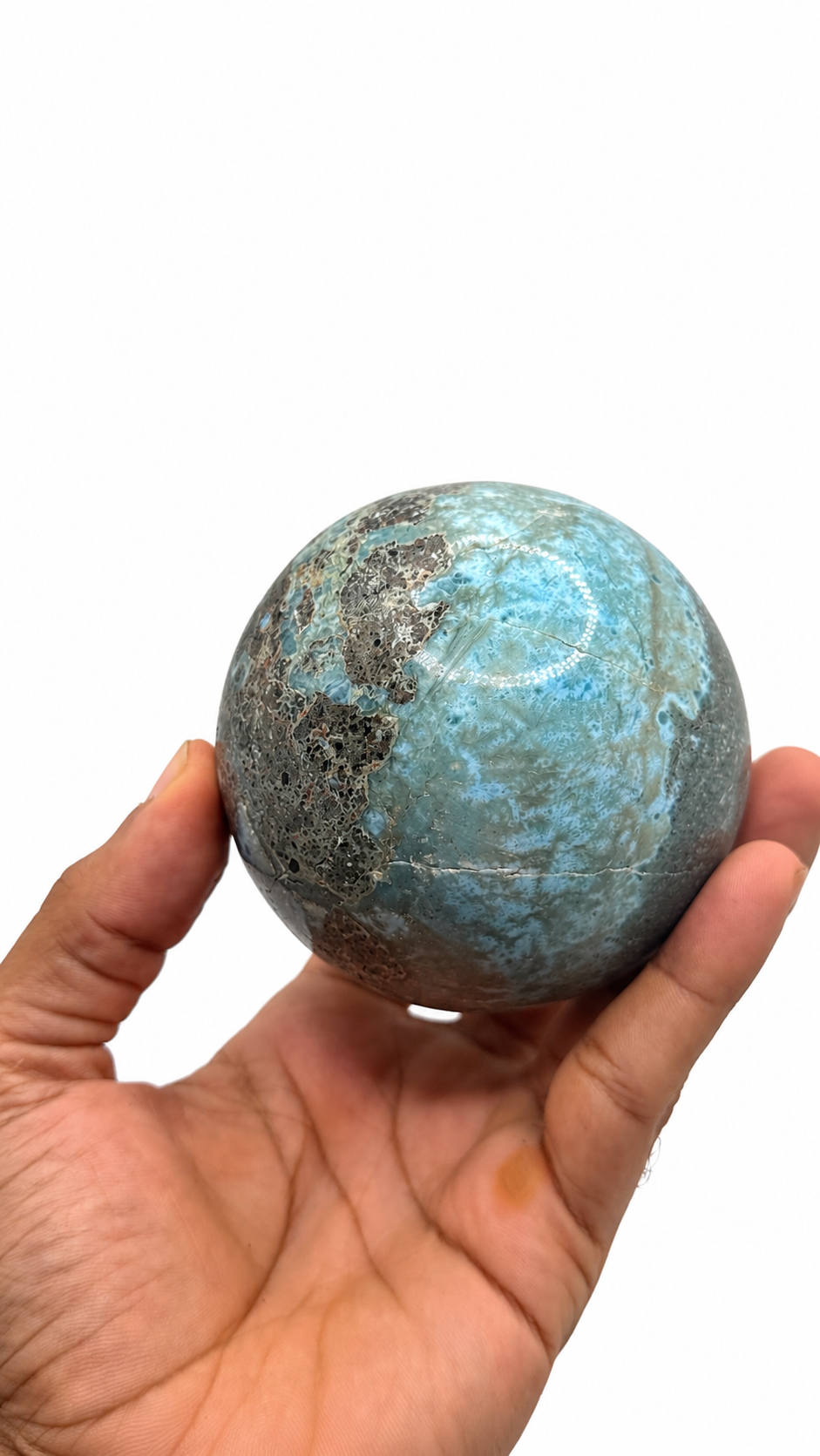 A hand holding a polished larimar stone sphere with natural marbled patterns, shown against a plain white background.